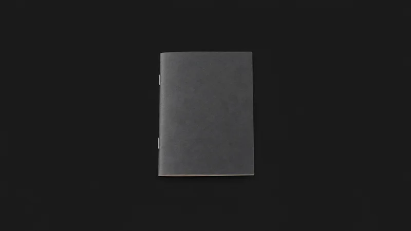 Isolated a saddle-stitched booklet with a folded cover centred on a seamless deep charcoal near-black studio background, generous empty margin on every side for overlaid branding