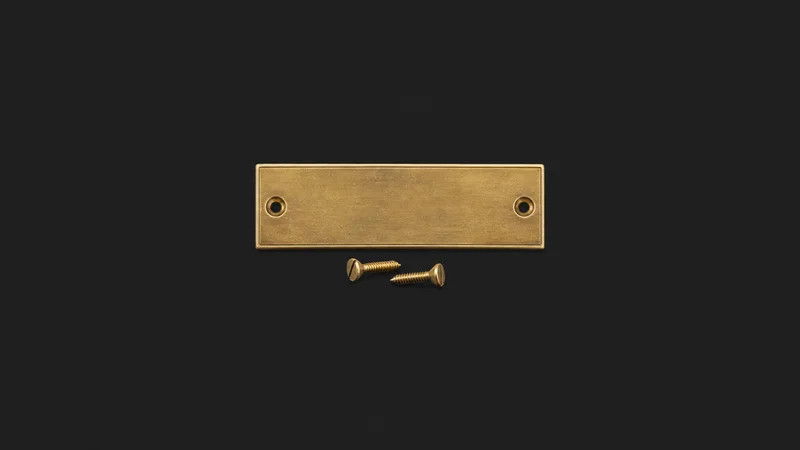 Isolated a brass door number plate with two loose screws centred on a seamless deep charcoal near-black studio background, generous empty margin on every side for overlaid branding