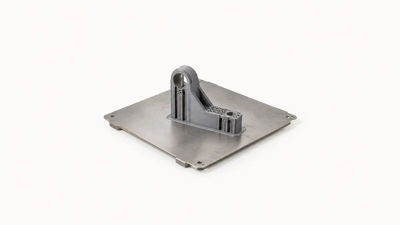 Isolated a bare steel build plate with a half-finished printed bracket adhered to it centred on a seamless pale off-white studio background, generous empty margin on every side for overlaid branding