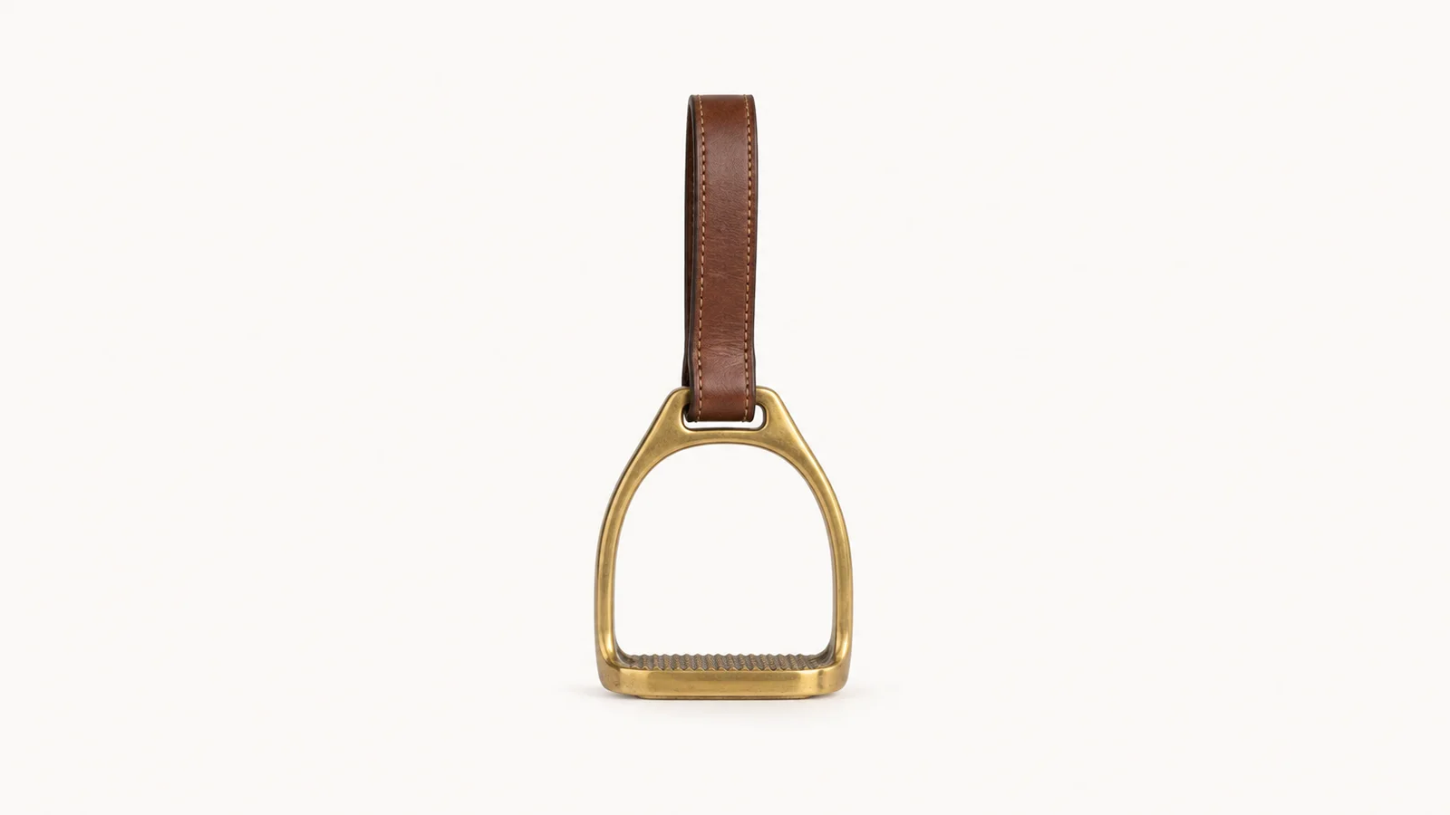 Isolated a brass stirrup iron on a leather stirrup strap centred on a seamless pale off-white studio background, generous empty margin on every side for overlaid branding