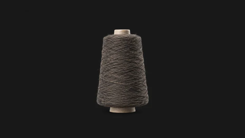 Isolated a cone of spun wool yarn on a spindle centred on a seamless deep charcoal near-black studio background, generous empty margin on every side for overlaid branding