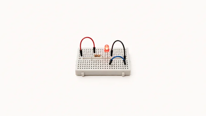 Isolated a breadboard wired with jumper leads and an LED centred on a seamless pale off-white studio background, generous empty margin on every side for overlaid branding