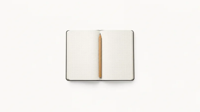 Isolated a grid-ruled dot notebook opened flat with a pencil centred on a seamless pale off-white studio background, generous empty margin on every side for overlaid branding
