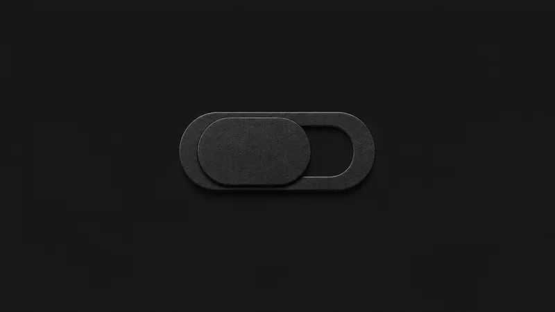 Isolated a matte-black privacy webcam cover slider centred on a seamless deep charcoal near-black studio background, generous empty margin on every side for overlaid branding