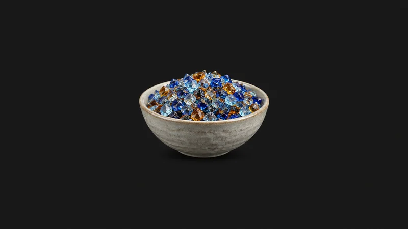 Isolated a bowl of crushed coloured glass frit in blue and amber centred on a seamless deep charcoal near-black studio background, generous empty margin on every side for overlaid branding