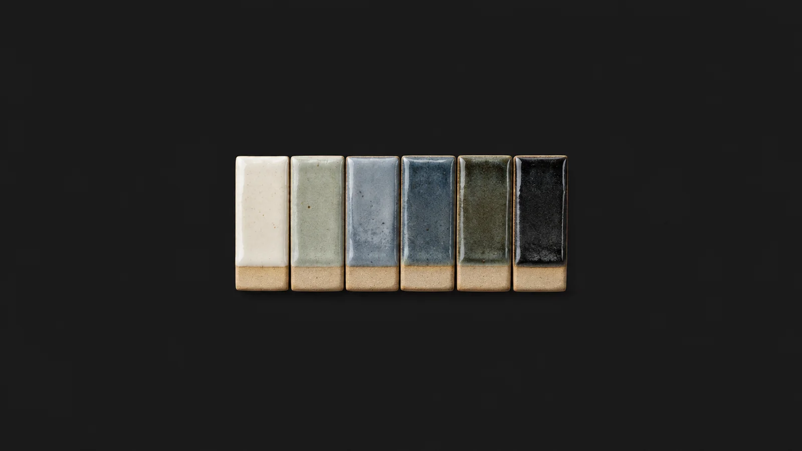 Isolated a set of glaze test tiles in graduated colours centred on a seamless deep charcoal near-black studio background, generous empty margin on every side for overlaid branding