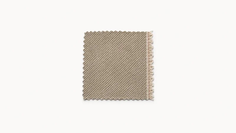 Isolated a swatch of twill fabric with a raw selvedge centred on a seamless pale off-white studio background, generous empty margin on every side for overlaid branding