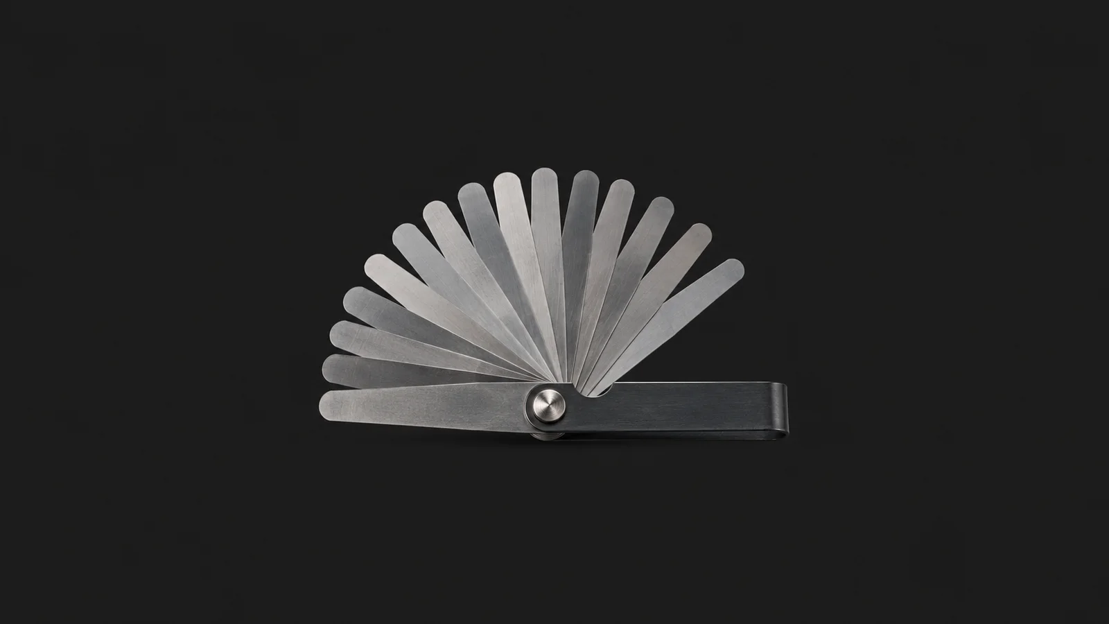 Isolated a set of feeler gauges fanned open centred on a seamless deep charcoal near-black studio background, generous empty margin on every side for overlaid branding