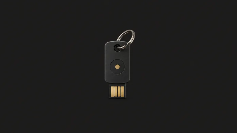 Isolated a hardware security key on a lanyard ring centred on a seamless deep charcoal near-black studio background, generous empty margin on every side for overlaid branding