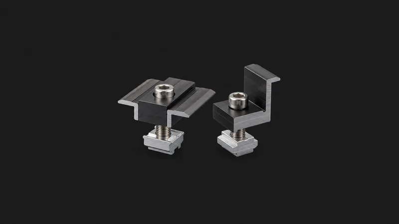 Isolated an aluminium mid-clamp and end-clamp set for panel rails centred on a seamless deep charcoal near-black studio background, generous empty margin on every side for overlaid branding