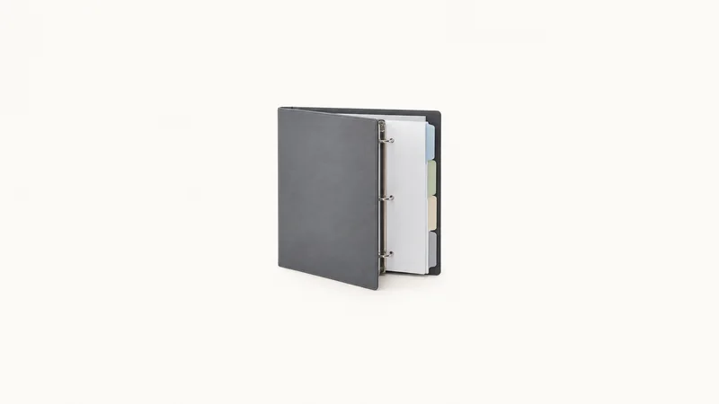 Isolated a ring binder of blank tabbed dividers centred on a seamless pale off-white studio background, generous empty margin on every side for overlaid branding