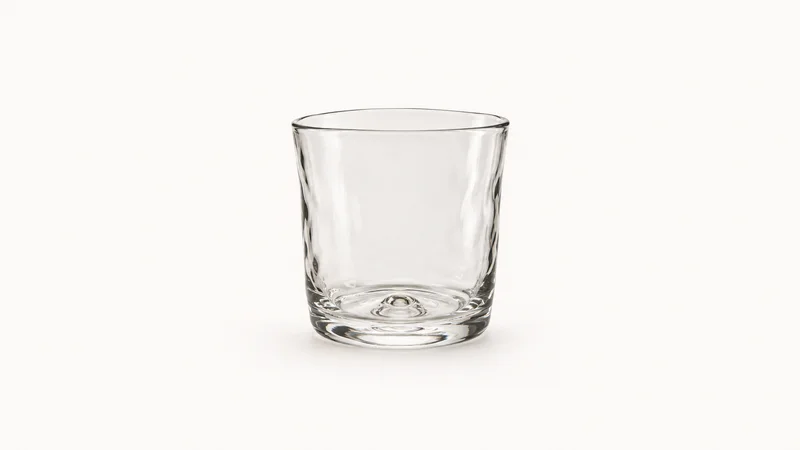 Isolated a hand-blown clear glass tumbler with a pontil mark on its base centred on a seamless pale off-white studio background, generous empty margin on every side for overlaid branding