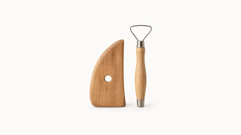 Isolated a wooden throwing rib and loop trimming tool pair centred on a seamless pale off-white studio background, generous empty margin on every side for overlaid branding