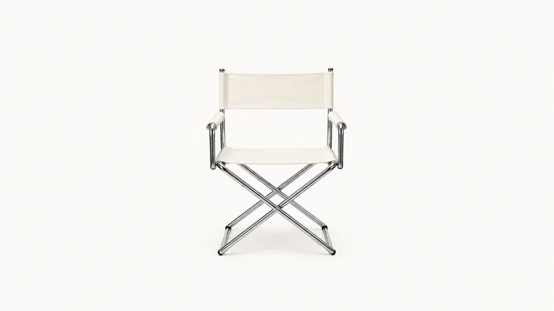 Isolated a chrome-legged director's chair with a blank canvas seat centred on a seamless pale off-white studio background, generous empty margin on every side for overlaid branding