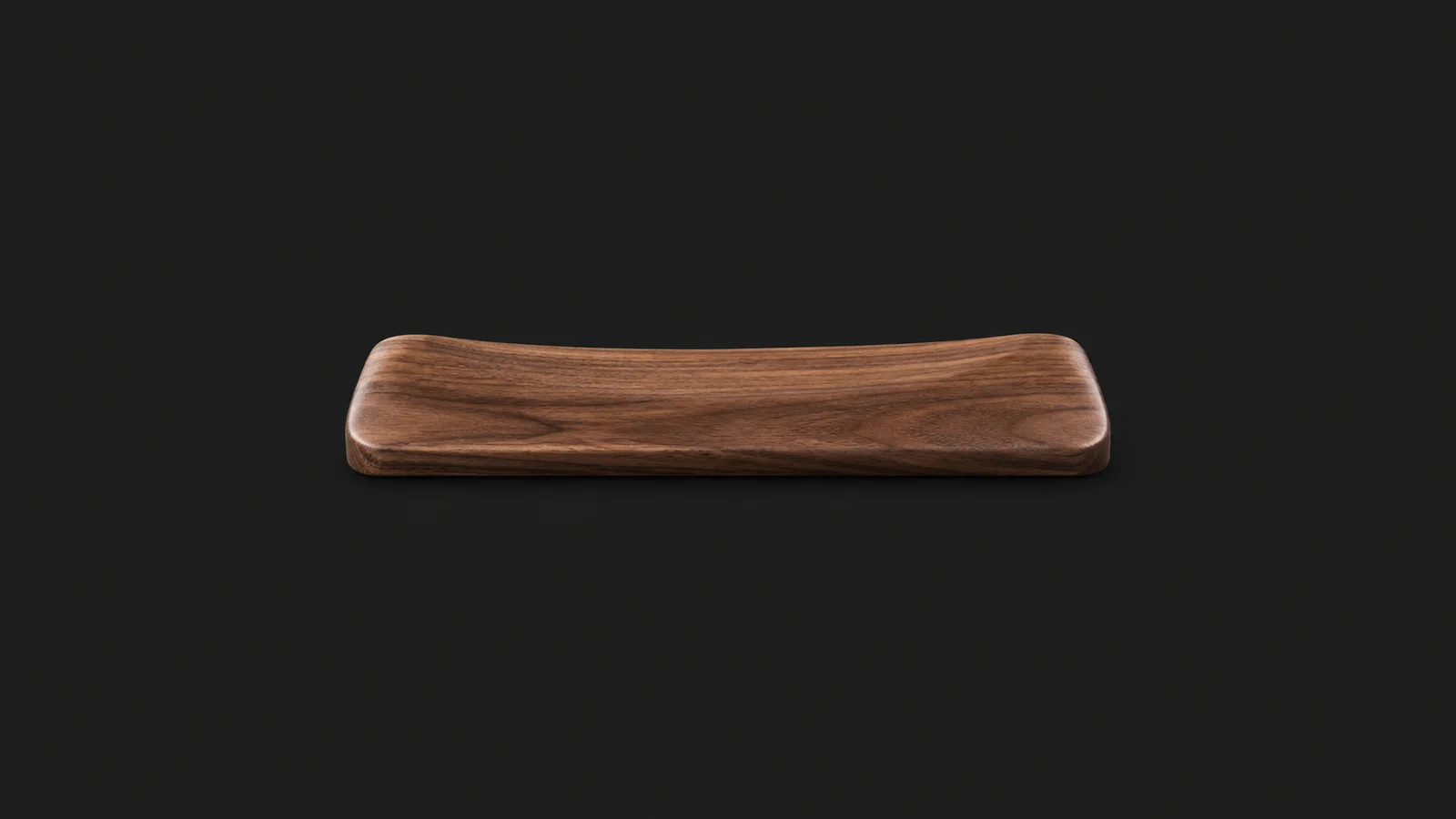 Isolated a wrist rest of oiled walnut centred on a seamless deep charcoal near-black studio background, generous empty margin on every side for overlaid branding