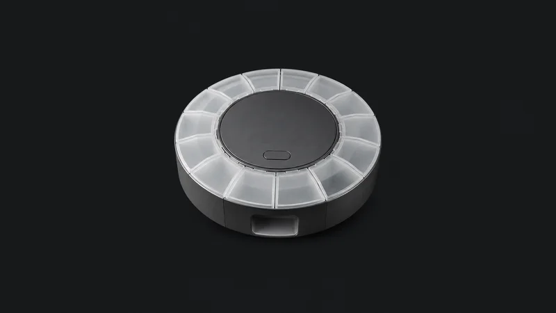 Isolated a smart pill dispenser with a ring of compartments and a blank front panel centred on a seamless deep charcoal near-black studio background, generous empty margin on every side for overlaid branding