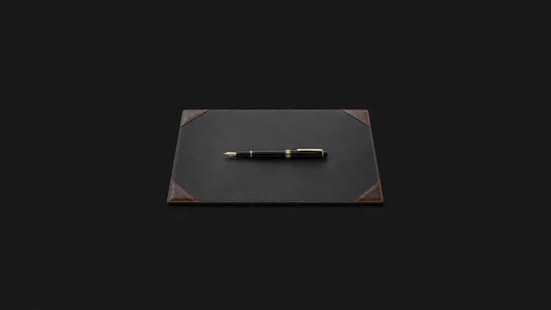 Isolated a leather-cornered desk blotter with a fountain pen centred on a seamless deep charcoal near-black studio background, generous empty margin on every side for overlaid branding