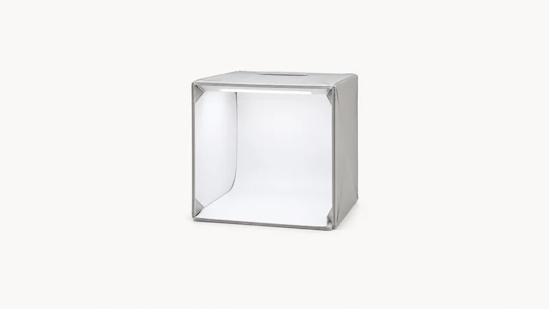 Isolated a folding tabletop photography lightbox centred on a seamless pale off-white studio background, generous empty margin on every side for overlaid branding
