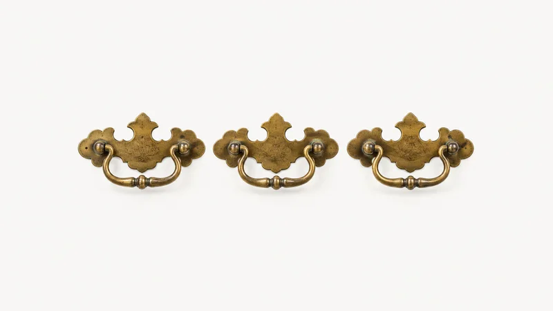 Isolated a set of antique brass drawer pulls with backplates laid in a row centred on a seamless pale off-white studio background, generous empty margin on every side for overlaid branding