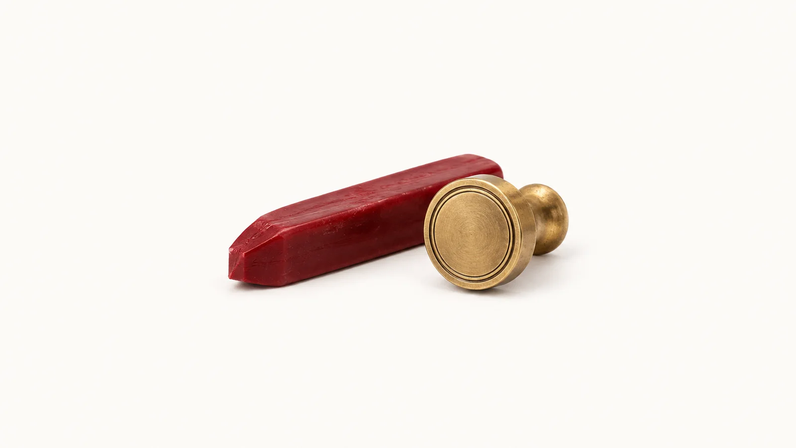 Isolated a stick of red sealing wax and a brass seal matrix centred on a seamless pale off-white studio background, generous empty margin on every side for overlaid branding