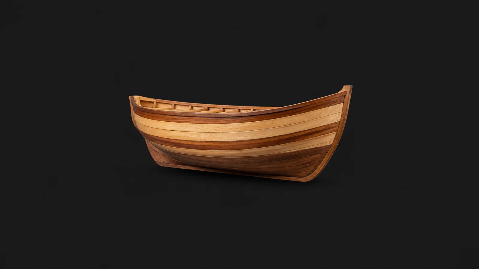 Isolated a half-model boat hull carved in lifts of alternating timber centred on a seamless deep charcoal near-black studio background, generous empty margin on every side for overlaid branding