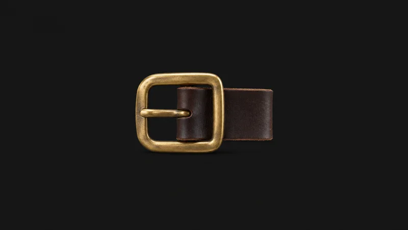 Isolated a brass belt buckle on a strip of unstitched bridle leather centred on a seamless deep charcoal near-black studio background, generous empty margin on every side for overlaid branding