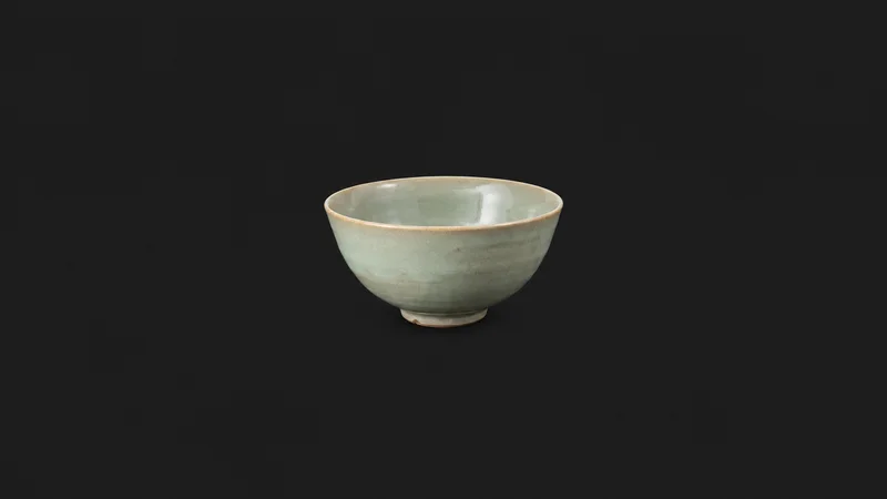 Isolated a hand-thrown porcelain bowl with a celadon glaze centred on a seamless deep charcoal near-black studio background, generous empty margin on every side for overlaid branding