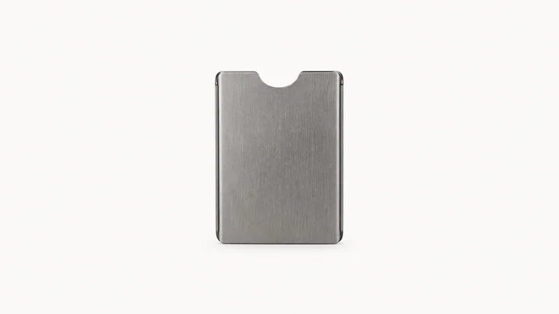 Isolated a RFID-blocking metal card sleeve centred on a seamless pale off-white studio background, generous empty margin on every side for overlaid branding
