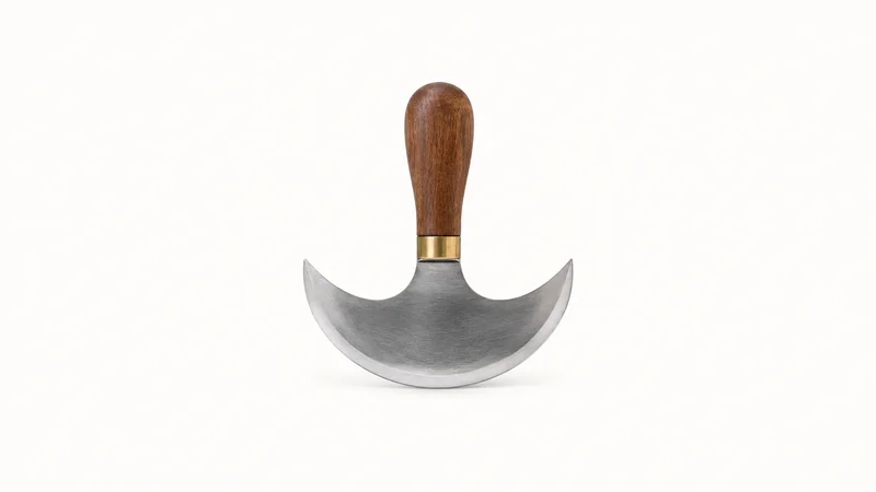 Isolated a saddler's half-moon head knife centred on a seamless pale off-white studio background, generous empty margin on every side for overlaid branding