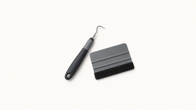 Isolated a vinyl weeding hook and squeegee pair centred on a seamless pale off-white studio background, generous empty margin on every side for overlaid branding