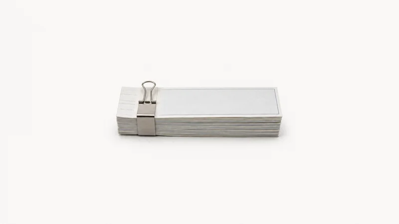 Isolated a bundle of blank cheque stubs bound with a clip centred on a seamless pale off-white studio background, generous empty margin on every side for overlaid branding