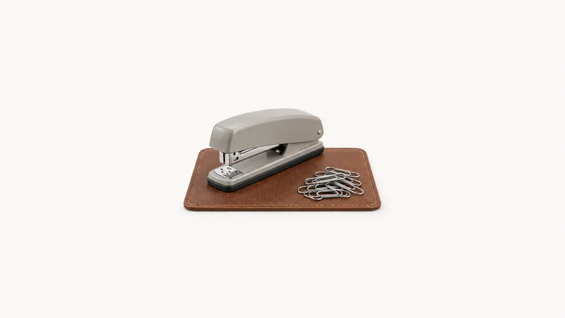 Isolated a bundle of paper clips and a stapler on a leather mat centred on a seamless pale off-white studio background, generous empty margin on every side for overlaid branding