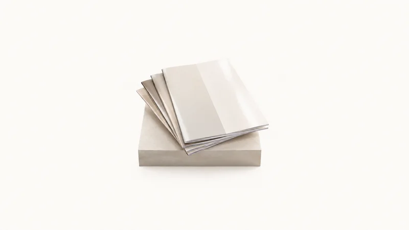 Isolated a stack of glossy blank property brochures fanned on a plinth centred on a seamless pale off-white studio background, generous empty margin on every side for overlaid branding