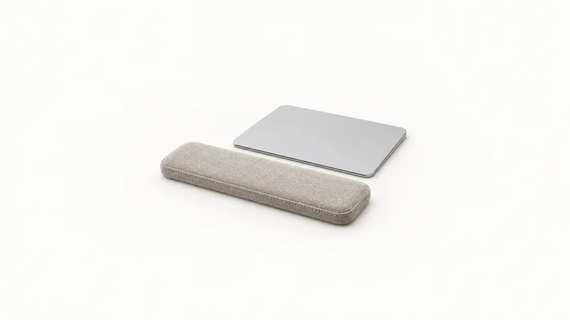 Isolated a wrist rest of stitched fabric beside a trackpad centred on a seamless pale off-white studio background, generous empty margin on every side for overlaid branding