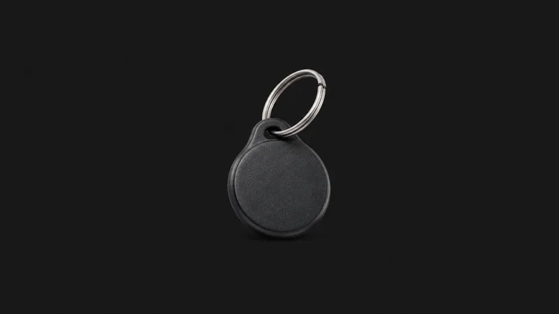 Isolated a coin-sized NFC payment fob on a steel ring centred on a seamless deep charcoal near-black studio background, generous empty margin on every side for overlaid branding