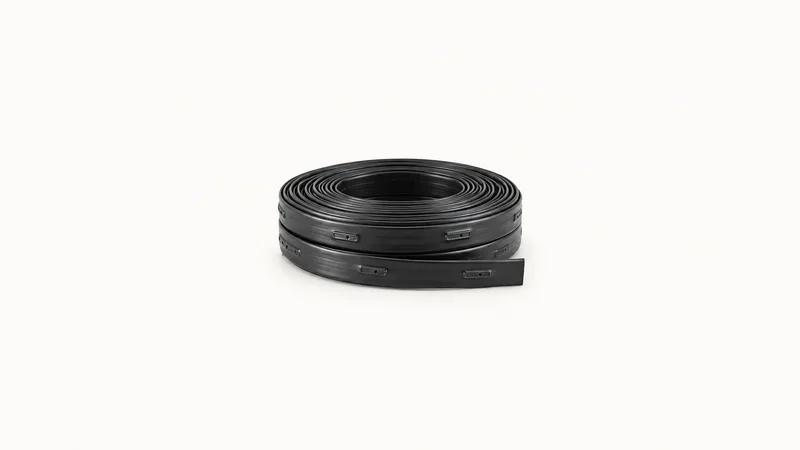 Isolated a coiled length of drip-irrigation tape with punched emitters centred on a seamless pale off-white studio background, generous empty margin on every side for overlaid branding