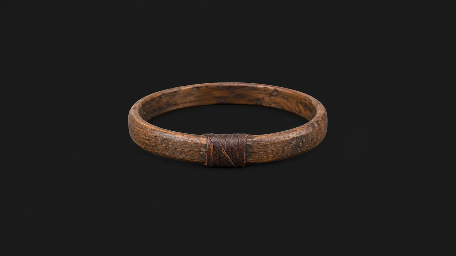 Isolated a wooden mast hoop with a leather-wrapped seizing centred on a seamless deep charcoal near-black studio background, generous empty margin on every side for overlaid branding