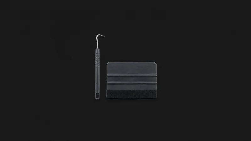 Isolated a vinyl weeding hook and squeegee pair centred on a seamless deep charcoal near-black studio background, generous empty margin on every side for overlaid branding