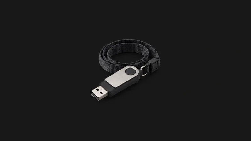 Isolated a bootable recovery drive on a coiled lanyard centred on a seamless deep charcoal near-black studio background, generous empty margin on every side for overlaid branding