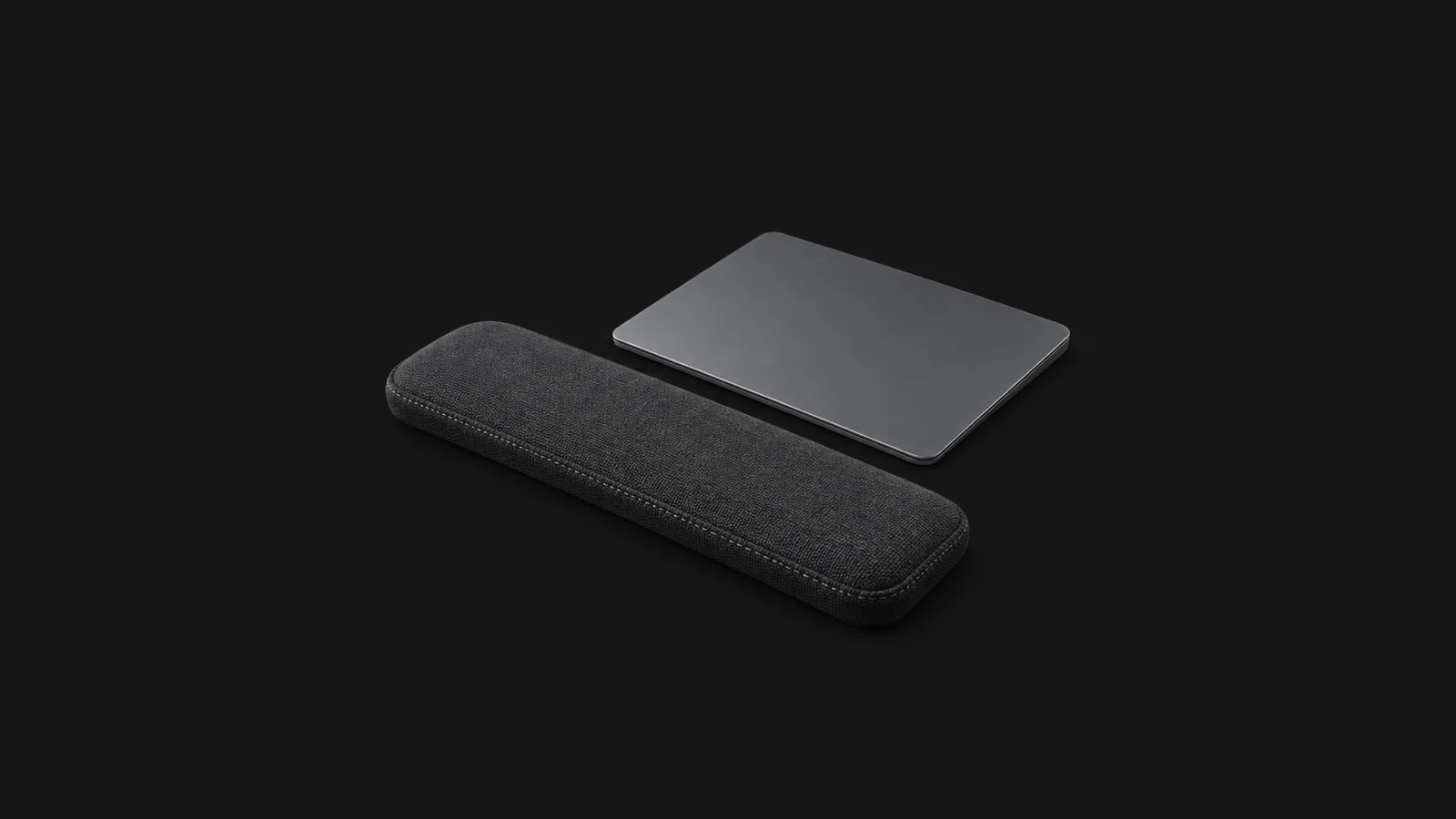 Isolated a wrist rest of stitched fabric beside a trackpad centred on a seamless deep charcoal near-black studio background, generous empty margin on every side for overlaid branding
