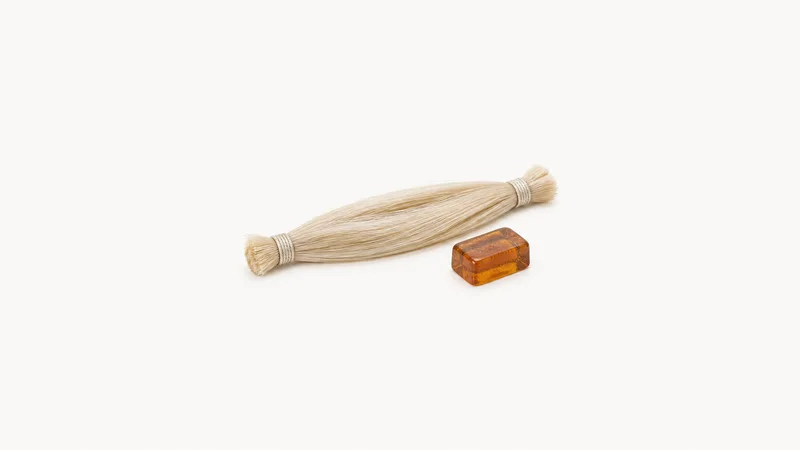 Isolated a horsehair bow hank bound at both ends beside a block of rosin centred on a seamless pale off-white studio background, generous empty margin on every side for overlaid branding