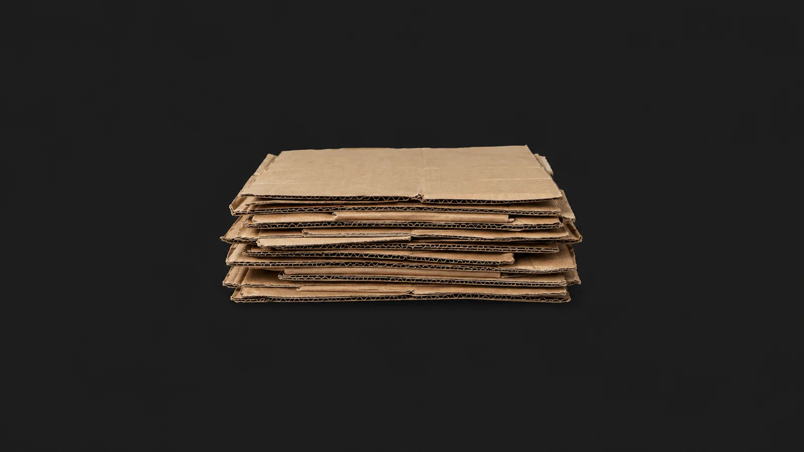 Isolated a stack of flattened recovered corrugated sheets centred on a seamless deep charcoal near-black studio background, generous empty margin on every side for overlaid branding