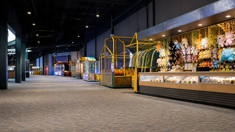 Wide interior view of a arcade and games midway hall with no people, soft even indoor light, clean uncluttered foreground for text
