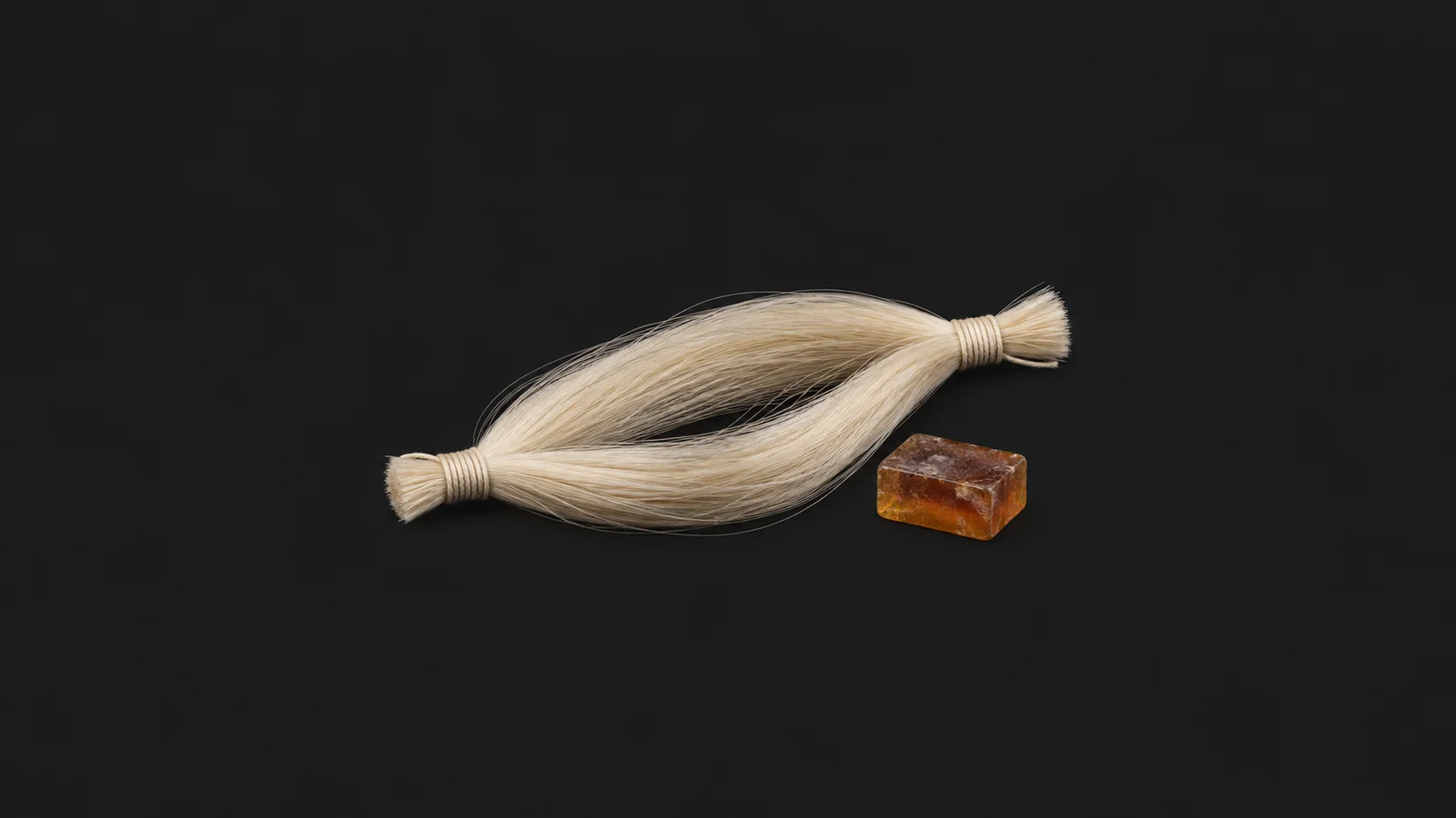 Isolated a horsehair bow hank bound at both ends beside a block of rosin centred on a seamless deep charcoal near-black studio background, generous empty margin on every side for overlaid branding