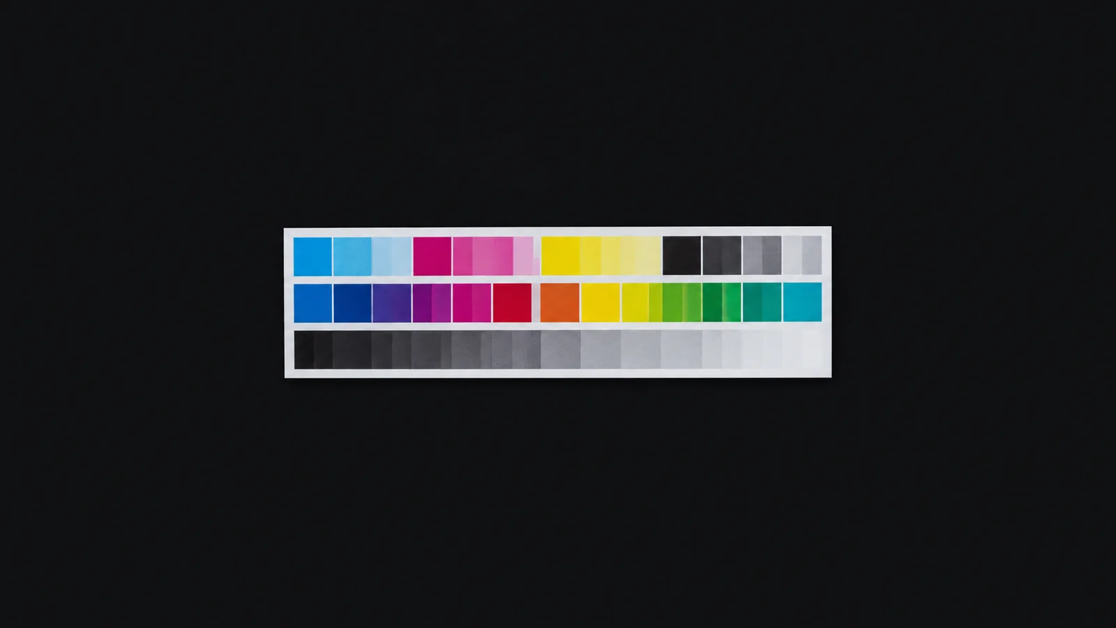 Isolated a printer colour-calibration test strip with density patches centred on a seamless deep charcoal near-black studio background, generous empty margin on every side for overlaid branding