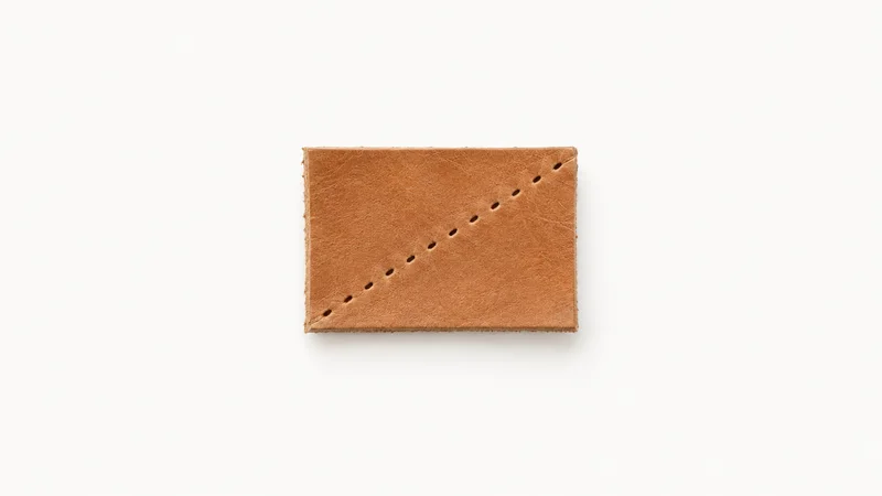 Abstract a diagonal row of saddle-stitch holes running across a tan leather plane motif centred on a seamless pale off-white studio background, generous empty margin for overlaid branding