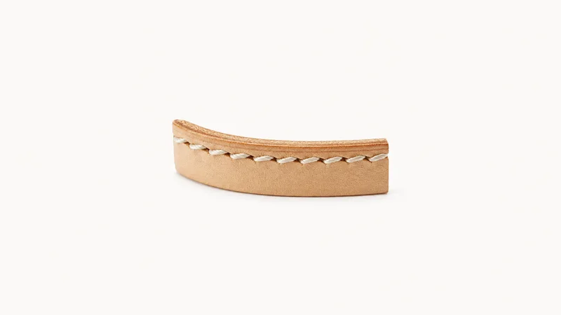 Abstract a row of saddle stitches running along a leather edge motif centred on a seamless pale off-white studio background, generous empty margin for overlaid branding