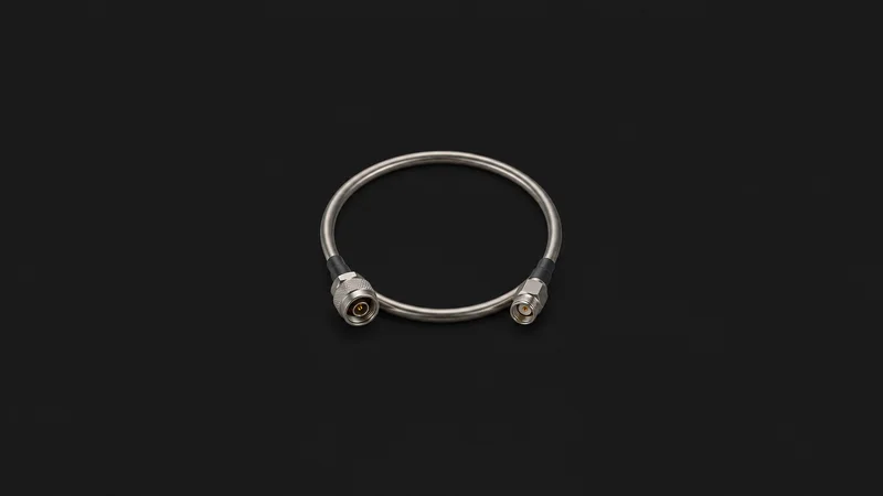 Isolated a coaxial semi-rigid cable bent into a loop centred on a seamless deep charcoal near-black studio background, generous empty margin on every side for overlaid branding