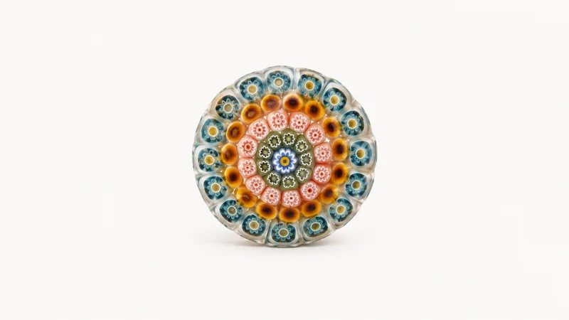 Abstract concentric rings of coloured glass cane in a millefiori pattern motif centred on a seamless pale off-white studio background, generous empty margin for overlaid branding