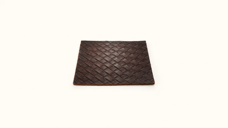 Abstract a basketweave stamp pattern receding in perspective across dark leather motif centred on a seamless pale off-white studio background, generous empty margin for overlaid branding